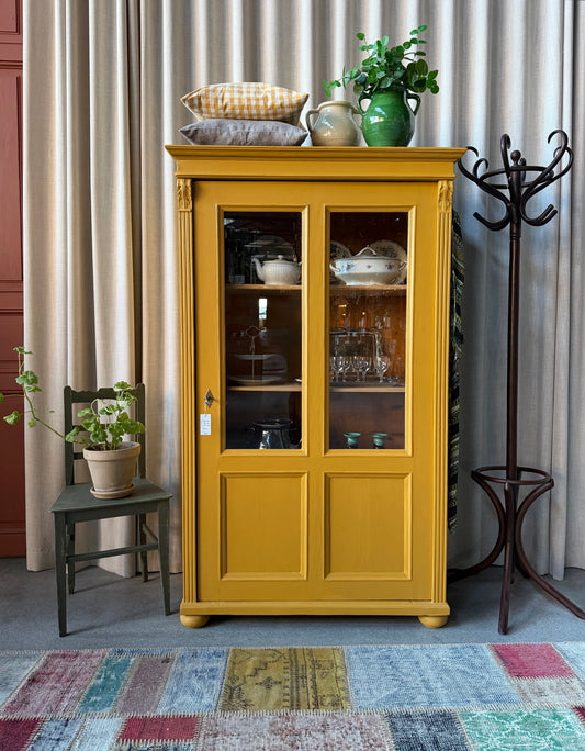 Ett gammalt vackert vitrinskåp med två vitrin glas och täckt spegel nedtill. Skåpet har en högerhängd dörr och fina detaljer. 