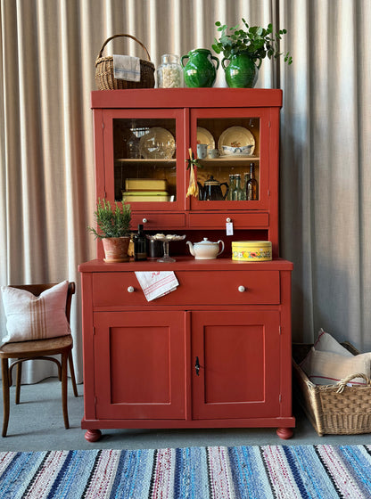 Ett gammalt, vackert och charmigt köksskåp i varmröd kulör med härlig utformning.