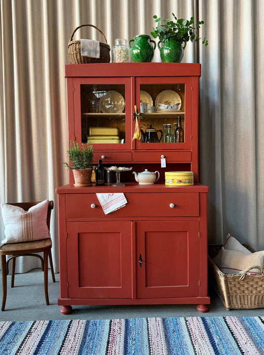 Ett gammalt, vackert och charmigt köksskåp i varmröd kulör med härlig utformning.
