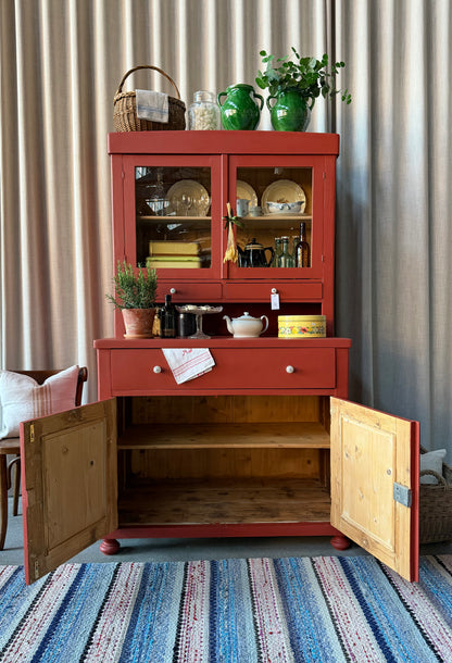 Ett gammalt, vackert och charmigt köksskåp i varmröd kulör med härlig utformning.