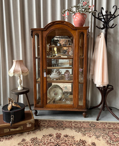 Ett gammalt, elegant vitrinskåp/displayskåp med ett stort glas samt glas i sidan för vackert ljusinsläpp. På skåpets insida sitter en spegel. 