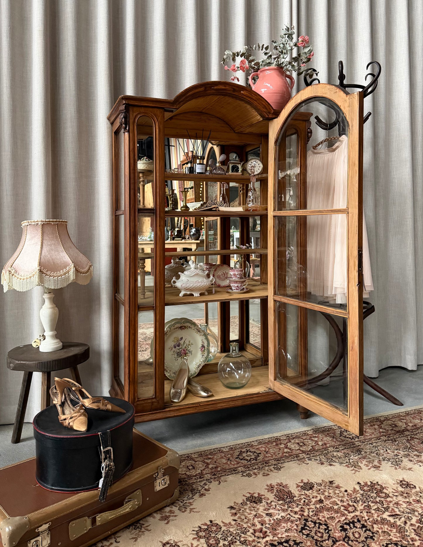 Ett gammalt, elegant vitrinskåp/displayskåp med ett stort glas samt glas i sidan för vackert ljusinsläpp. På skåpets insida sitter en spegel. 