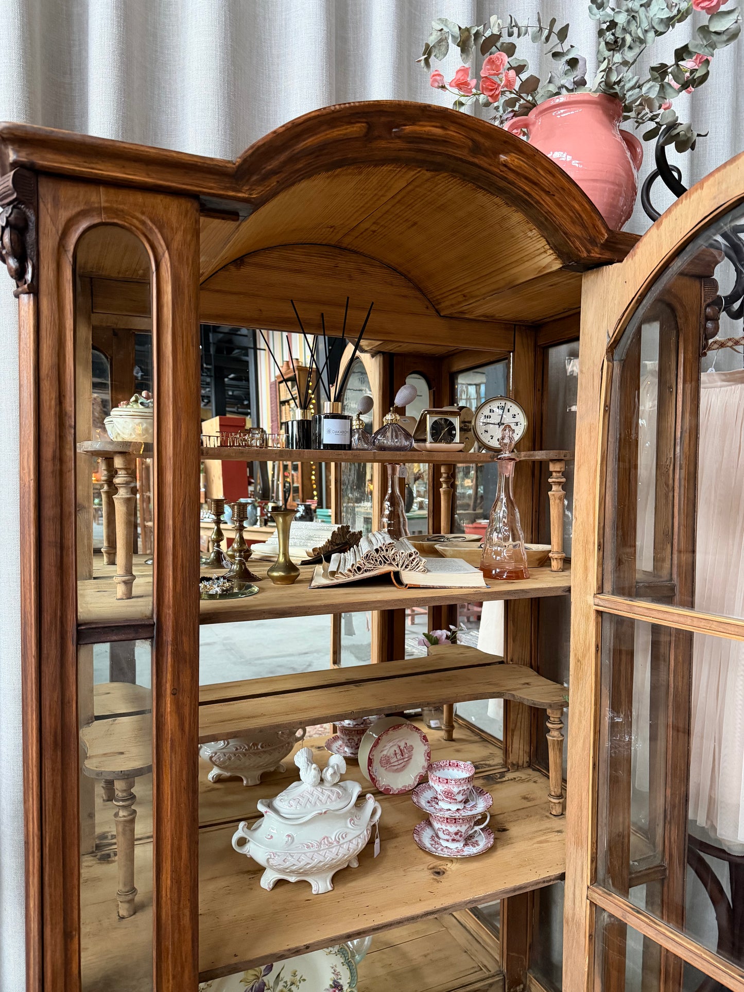 Ett gammalt, elegant vitrinskåp/displayskåp med ett stort glas samt glas i sidan för vackert ljusinsläpp. På skåpets insida sitter en spegel. 