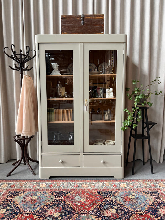 Ett vackert gammalt vitrinskåp med raka former, rundade krön och hela glaspartier i dörrarna. 