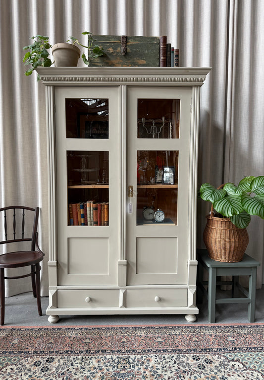 Ett gammalt vackert vitrinskåp med många fina och klassiska detaljer. Skåpet har vitringlas i dörrarna och dold förvaring nedtill samt två små praktiska lådor med inmålade träknoppar. 