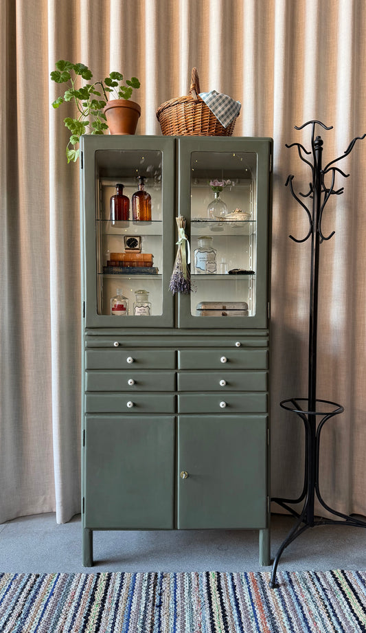 Ett gammalt läckert vitrinskåp/läkarskåp i trä med två hyllor i glas och även glas i sidan. Ett perfekt skåp för badrummet eller som vitrinskåp i kök eller vardagsrum. Skåpet har både en utdragbar skiva samt fina små lådor och skåp med dold förvaring nertill. Ett väldigt praktiskt skåp helt enkelt. Skåpet har fina tidstypiska porslinsknoppar och beslag. 