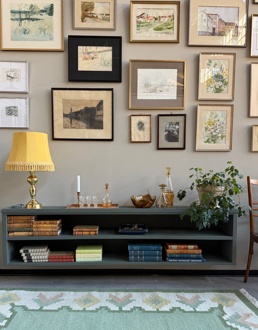 Denna tv-bänk/vägghängda hylla är nytillverkad i massiv furu på vårt snickeri i Ungern. Slutligen är den penselmålad med en matt vattenbaserad snickerifärg i Dakaboms mörka grå/gröna kulör. Väldigt fint att ha både tv-bänk och vitrinskåp i samma kulör, det blir en röd tråd och knyter ihop rummet fantastiskt fint. 