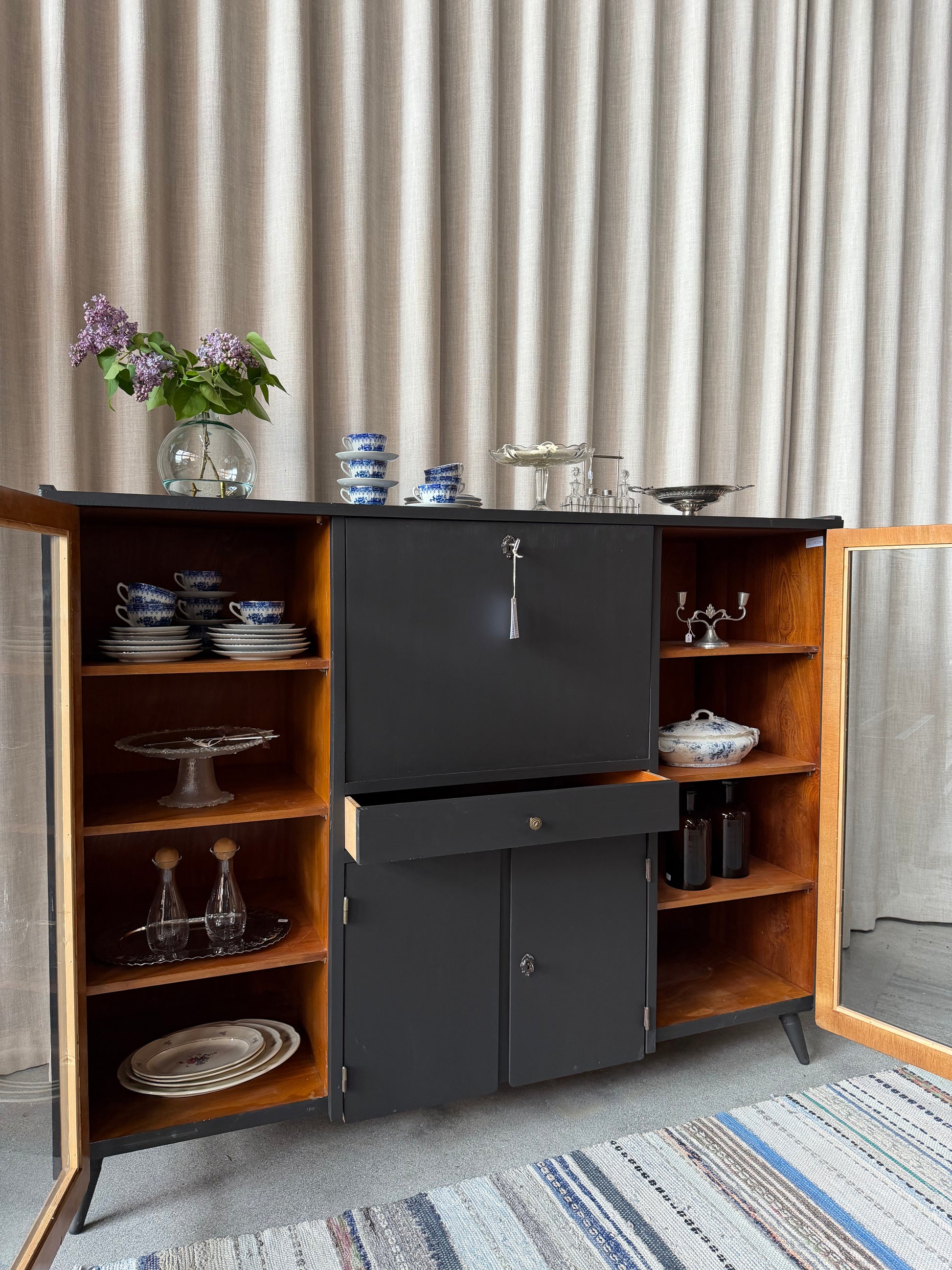 En gammal, elegant möbel som kan användas som skänk/sekretär/vitrinskåp. Perfekt för dig som önskar en både praktisk, elegant och otroligt charmig möbel där du kan "gömma undan" datorn i sekretären när du arbetat klart. Skåpet har i dagsläget flera hyllplan i vitrindelen samt en hylla i det täckta skåpet nedtill. Det finns även en liten låda. 