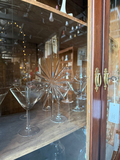 Ett elegant vitrinskåp i vacker Art Nouveau- stil med mjukt svängd front och utsmyckade detaljer som ger en tidlös och exklusiv känsla. Skåpet är tvådelat. Den övre vitrindelen med glasdörrar och hyllplan passar perfekt för att visa upp glas, porslin eller samlarföremål, medan den nedre delen är praktisk för förvaring. Skåpet har originalglas med dekorativ fasettslipning längs glasets kanter och tidstypiska slipade stjärnformade ornament. De mjuka formerna, gedigna hantverket och fantastiska detaljerna i vi