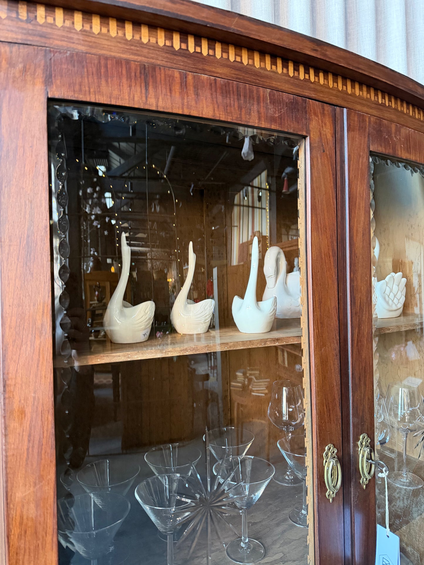 Ett elegant vitrinskåp i vacker Art Nouveau- stil med mjukt svängd front och utsmyckade detaljer som ger en tidlös och exklusiv känsla. Skåpet är tvådelat. Den övre vitrindelen med glasdörrar och hyllplan passar perfekt för att visa upp glas, porslin eller samlarföremål, medan den nedre delen är praktisk för förvaring. Skåpet har originalglas med dekorativ fasettslipning längs glasets kanter och tidstypiska slipade stjärnformade ornament. De mjuka formerna, gedigna hantverket och fantastiska detaljerna i vi