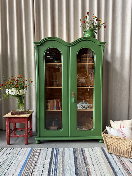 Ett gammalt unikt och charmigt vitrinskåp med vackra runda former i en klargrön färg. Vitrindörrarna lyfter fram ditt porslin, glas eller favoritböcker på ett elegant sätt, medan den gedigna formen, utsmyckningen och de mjuka detaljerna ger skåpet karaktär. Ett riktigt blickfång som lyfter rummet och passar såväl in i köket som vardagsrummet. Skåpet är varsamt renoverat och sedan penselmålat med en matt snickerifärg i Dakaboms klargröna kulör.