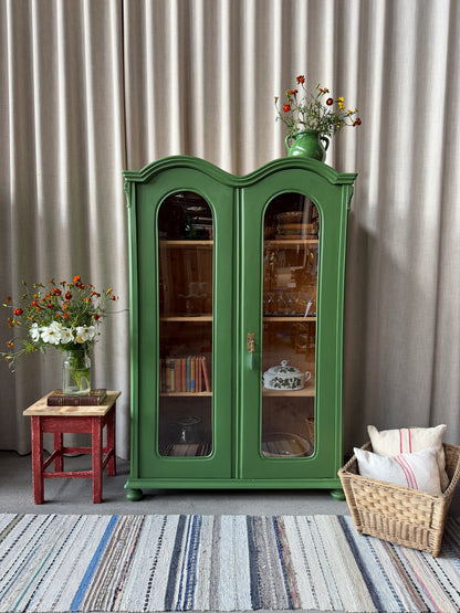 Ett gammalt unikt och charmigt vitrinskåp med vackra runda former i en klargrön färg. Vitrindörrarna lyfter fram ditt porslin, glas eller favoritböcker på ett elegant sätt, medan den gedigna formen, utsmyckningen och de mjuka detaljerna ger skåpet karaktär. Ett riktigt blickfång som lyfter rummet och passar såväl in i köket som vardagsrummet. Skåpet är varsamt renoverat och sedan penselmålat med en matt snickerifärg i Dakaboms klargröna kulör.