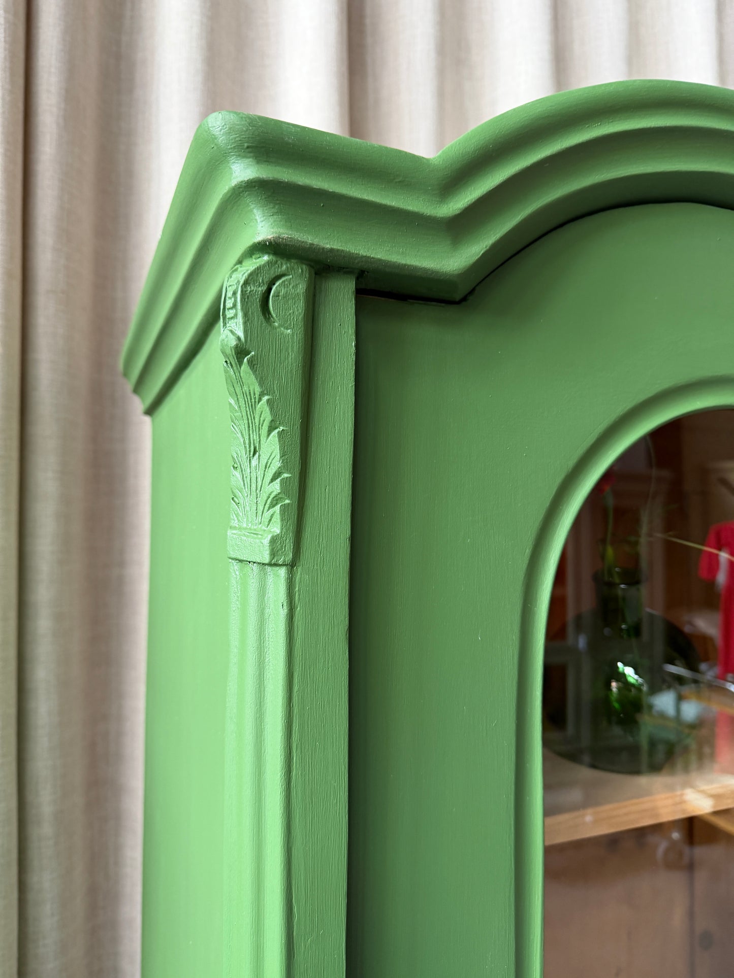 Detaljbild.Ett gammalt unikt och charmigt vitrinskåp med vackra runda former i en klargrön färg. Vitrindörrarna lyfter fram ditt porslin, glas eller favoritböcker på ett elegant sätt, medan den gedigna formen, utsmyckningen och de mjuka detaljerna ger skåpet karaktär. Ett riktigt blickfång som lyfter rummet och passar såväl in i köket som vardagsrummet. Skåpet är varsamt renoverat och sedan penselmålat med en matt snickerifärg i Dakaboms klargröna kulör.