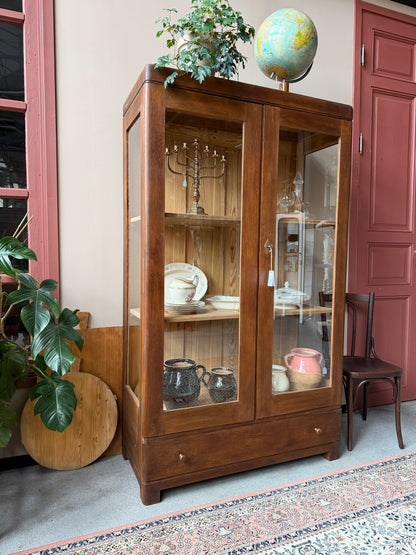 Ett gammalt, fantastiskt vackert vitrinskåp i fin nyans. Skåpet har två stora vitrindörrar samt glas i sidan för vackert ljusinsläpp. Det har 3 nya och fräscha hyllplan. Samt en bred låda nedtill. Det är varsamt renoverat och slutligen bestruken med en vax för skydd och fin yta.