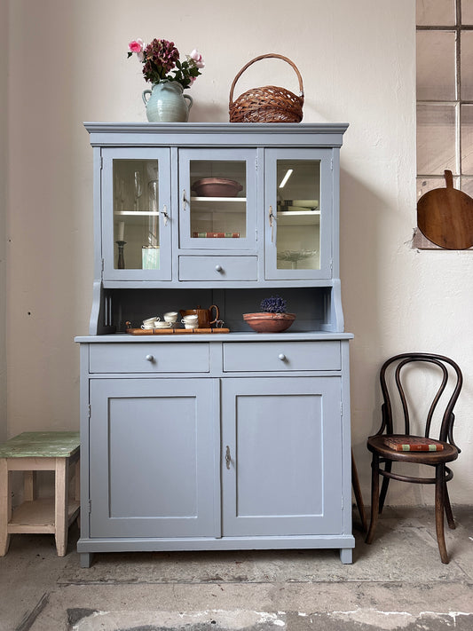 Bild visar ett gråblått köksskåp med vitrinluckor samt täckta luckor och lådor