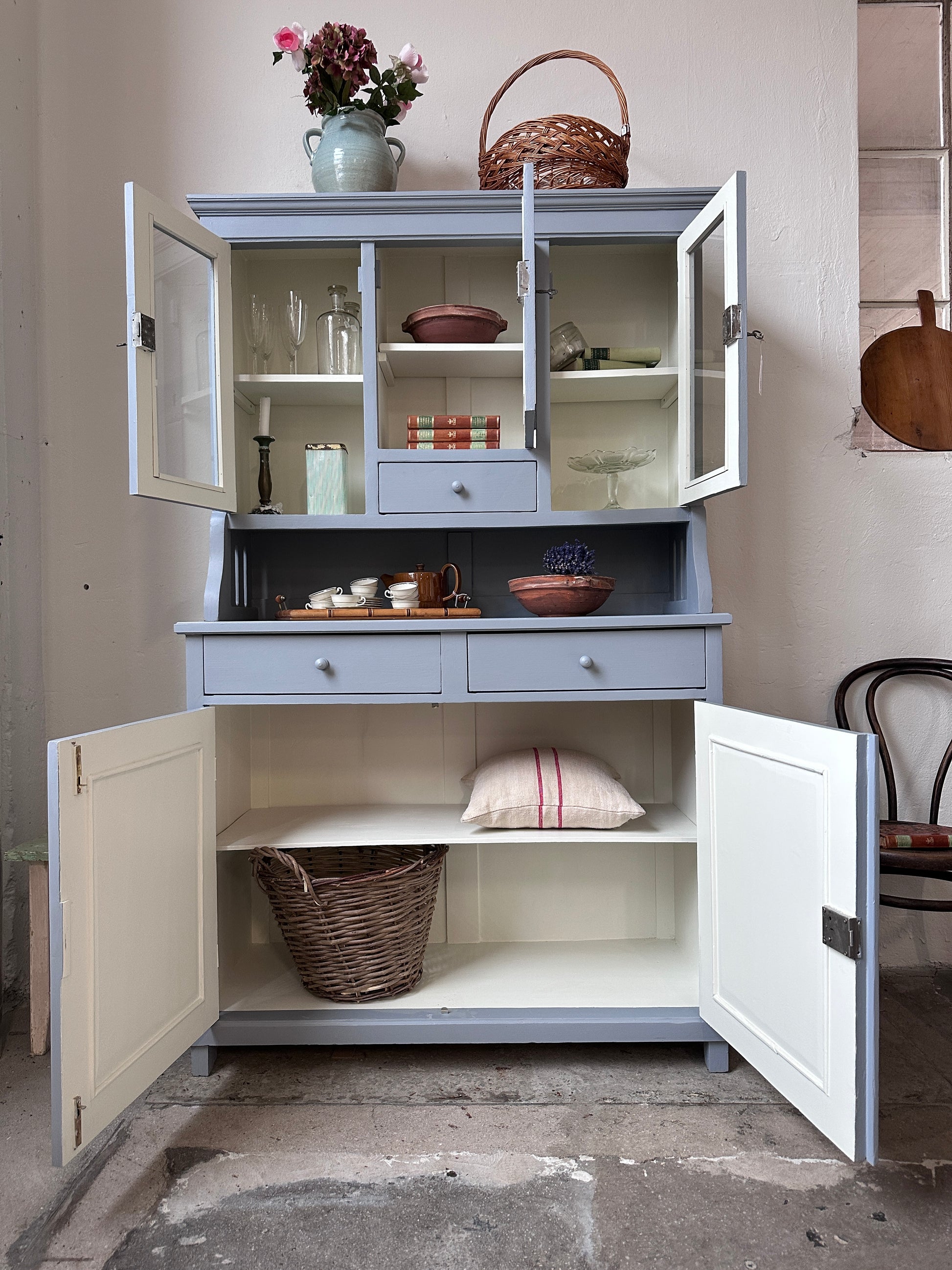 Bild visar ett gråblått köksskåp med vitrinluckor samt täckta luckor och lådor. Bild visar skåp med öppna dörrar.