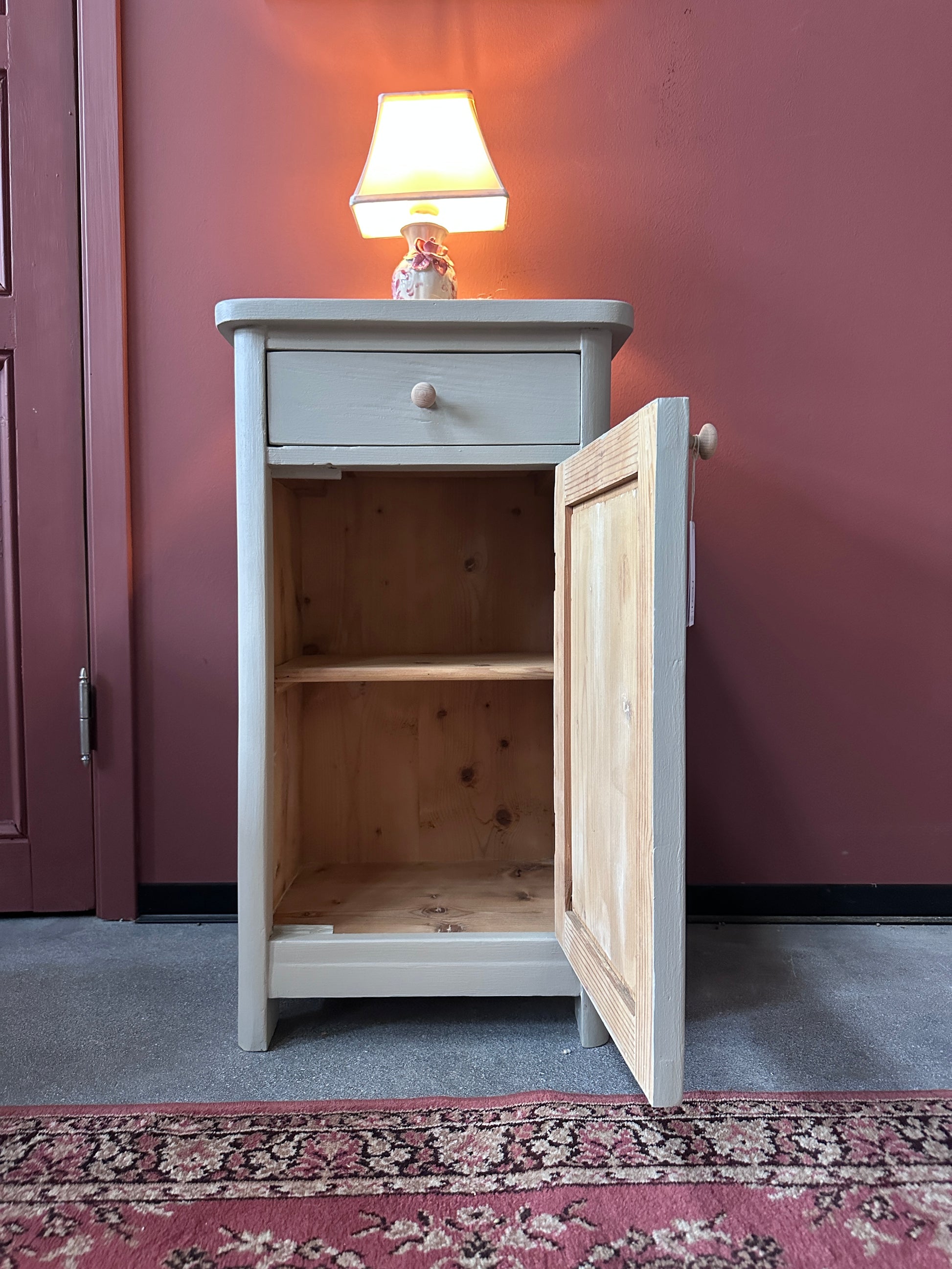 Gammalt målat sängbord mot en röd vägg.  Dörren står öppen.