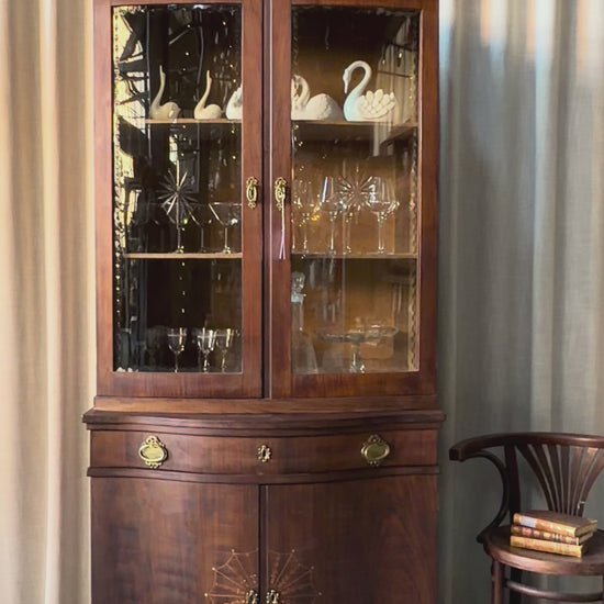 Ett elegant vitrinskåp i vacker Art Nouveau- stil med mjukt svängd front och utsmyckade detaljer som ger en tidlös och exklusiv känsla. Skåpet är tvådelat. Den övre vitrindelen med glasdörrar och hyllplan passar perfekt för att visa upp glas, porslin eller samlarföremål, medan den nedre delen är praktisk för förvaring. Skåpet har originalglas med dekorativ fasettslipning längs glasets kanter och tidstypiska slipade stjärnformade ornament. De mjuka formerna, gedigna hantverket och fantastiska detaljerna i vi