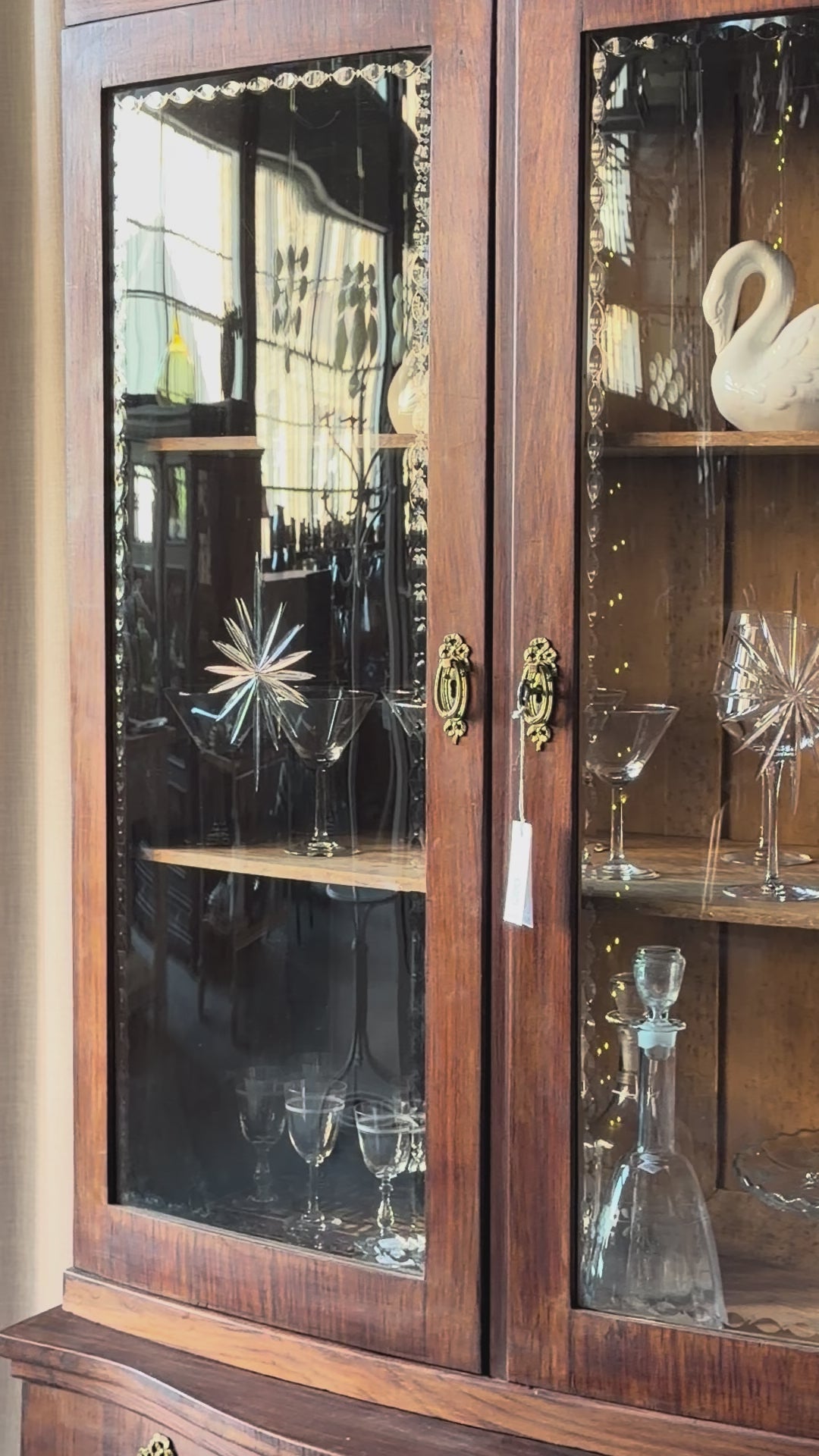 Ett elegant vitrinskåp i vacker Art Nouveau- stil med mjukt svängd front och utsmyckade detaljer som ger en tidlös och exklusiv känsla. Skåpet är tvådelat. Den övre vitrindelen med glasdörrar och hyllplan passar perfekt för att visa upp glas, porslin eller samlarföremål, medan den nedre delen är praktisk för förvaring. Skåpet har originalglas med dekorativ fasettslipning längs glasets kanter och tidstypiska slipade stjärnformade ornament. De mjuka formerna, gedigna hantverket och fantastiska detaljerna i vi