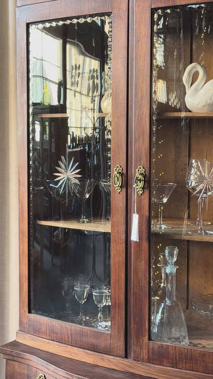 Ett elegant vitrinskåp i vacker Art Nouveau- stil med mjukt svängd front och utsmyckade detaljer som ger en tidlös och exklusiv känsla. Skåpet är tvådelat. Den övre vitrindelen med glasdörrar och hyllplan passar perfekt för att visa upp glas, porslin eller samlarföremål, medan den nedre delen är praktisk för förvaring. Skåpet har originalglas med dekorativ fasettslipning längs glasets kanter och tidstypiska slipade stjärnformade ornament. De mjuka formerna, gedigna hantverket och fantastiska detaljerna i vi