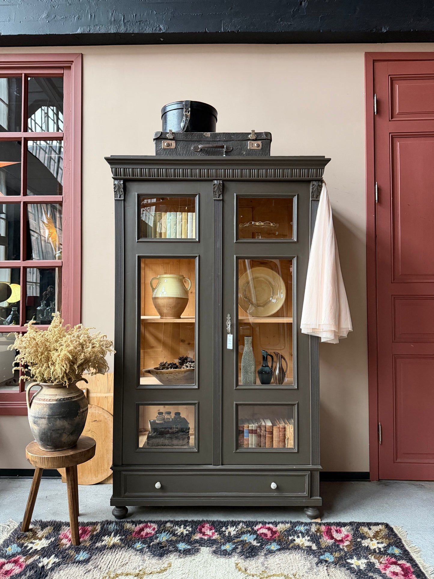 Ett gammalt, fantastiskt vackert vitrinskåp med fina detaljer i de raka formerna och det arbetade krönet. Skåpet har i dagsläget 3 st nya och fräscha hyllplan.Det har dessutom en bred praktisk låda längst ner med vackra porslinsknoppar. Skåpet är varsamt renoverat och slutligen penselmålat med en matt, vattenbaserad snickerifärg i en brun/grå kulör. 