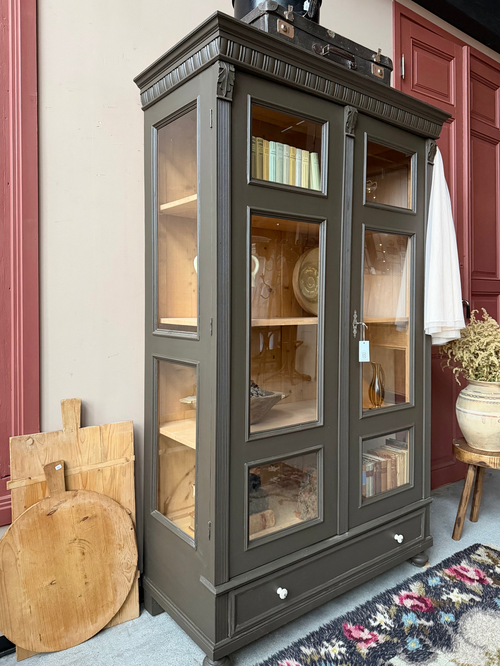 Ett gammalt, fantastiskt vackert vitrinskåp med fina detaljer i de raka formerna och det arbetade krönet. Skåpet har i dagsläget 3 st nya och fräscha hyllplan.Det har dessutom en bred praktisk låda längst ner med vackra porslinsknoppar. Skåpet är varsamt renoverat och slutligen penselmålat med en matt, vattenbaserad snickerifärg i en brun/grå kulör. 